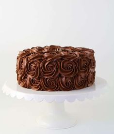 a chocolate cake sitting on top of a white cake platter with swirly frosting