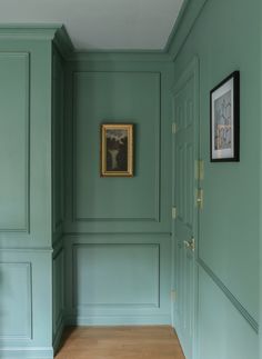 an empty room with green walls and wooden floors, framed pictures on the wall above