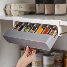 a person holding an open spice rack with spices in it on top of a shelf