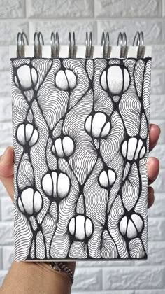 a hand holding up a notebook with black and white designs on it