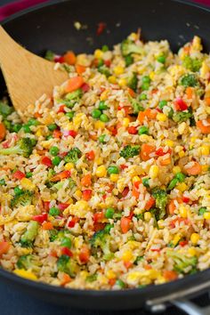 a skillet filled with rice and vegetables on top of a table next to a wooden spoon