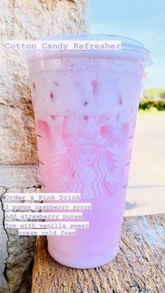 a pink drink sitting on top of a wooden table next to a stone wall with the caption cotton candy refresher