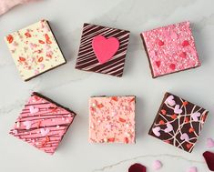 four different types of decorated chocolates on a white table with pink and red hearts