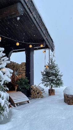 the porch is covered with snow and lit christmas trees are in the foreground, surrounded by logs