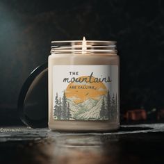 a candle is sitting on a table with mountains in the background and text that reads, the mountains are calling