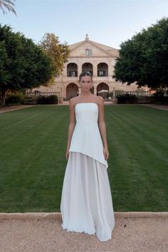 a woman is standing in front of a large building wearing a white dress and posing for the camera