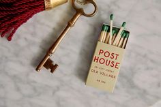 an antique key is sitting next to a box of matches and a red bag on a marble table