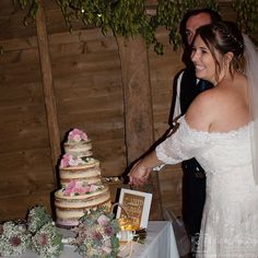 a bride and groom cutting their wedding cake at the end of their reception table in front of a wood paneled wall