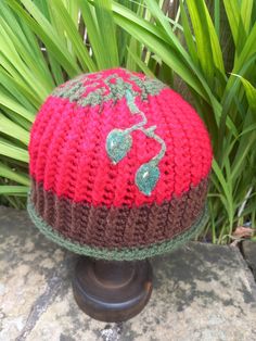 a red and brown knitted hat sitting on top of a stone