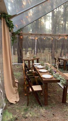 a dining table set up under a tent with candles and greenery on the tables