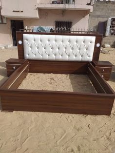 a wooden bed frame with white upholstered headboard and foot board in the sand