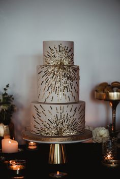 a white and gold wedding cake with lots of sparkles on the top, surrounded by candles