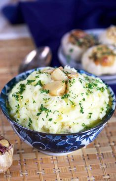 a bowl filled with mashed potatoes on top of a wooden table next to garlic and mushrooms