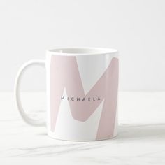 a coffee mug with the name michaela on it in pink and white colors, sitting on a marble surface