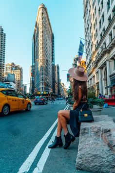 a woman sitting on a ledge in the middle of a busy city with tall buildings