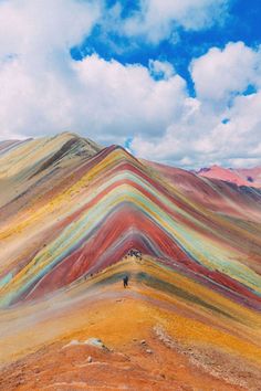 a man standing on top of a hill covered in rainbow colored hills under a cloudy blue sky