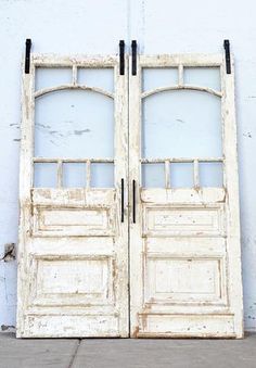 an old pair of double doors sitting on the side of a white building with no windows