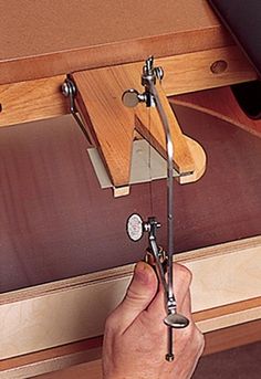 a hand holding a pair of scissors in front of a piece of wood and metal