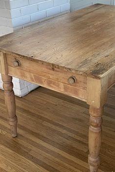 a wooden table sitting on top of a hard wood floor next to a brick wall