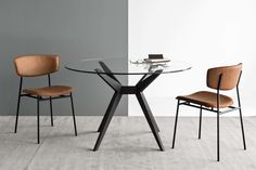 a glass table with two chairs and a book on it in front of a gray wall