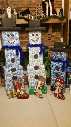 three snowmen made out of boxes sitting in front of a fire place with presents