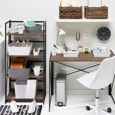 a desk with baskets and other items on it next to a wall mounted clock in a white room