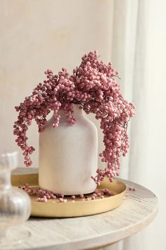 a white vase filled with pink flowers on top of a table