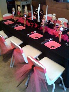 the table is decorated with barbie dolls and pink tulle skirted chairs, candles and decorations