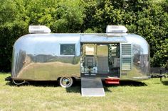 a silver trailer parked in the grass next to trees