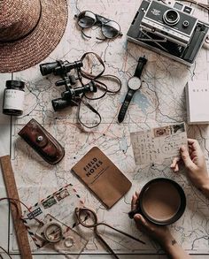 a person holding a coffee cup on top of a map with other items around it