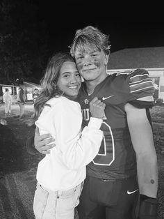 a young man and woman hugging each other in front of a football field at night