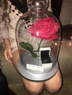 a person holding a cell phone in front of a glass vase with a flower inside