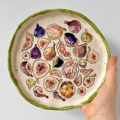 a hand holding a plate with different fruits and vegetables painted on the inside of it