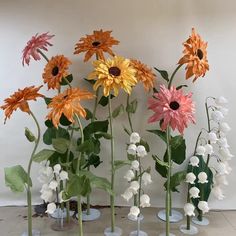 several vases filled with different types of flowers on top of a tile floor in front of a white wall