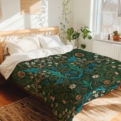 a bed with a green blanket on top of it next to a window and potted plant