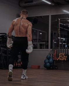 a man with no shirt and boxing gloves on is walking in the middle of a gym