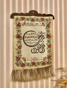 a wall hanging with an arabic calligraphy on it and some flowers in the background