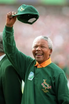 an older man holding up a green hat