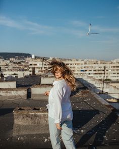 a woman standing on top of a roof with buildings in the backgrouds