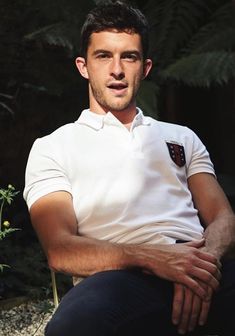 a man sitting on a rock with his arms crossed and looking at the camera while wearing a white polo shirt