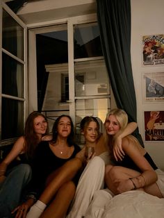 four women are sitting on a bed and one is holding a wine glass in her hand