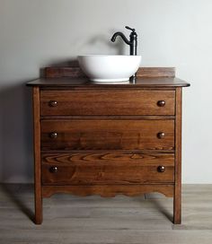 a bathroom sink sitting on top of a wooden dresser next to a white bowl and faucet