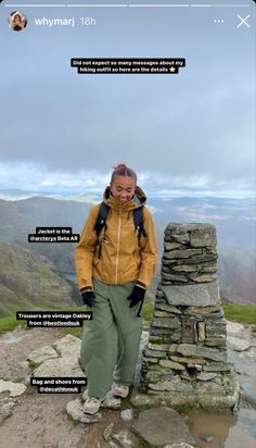 a woman standing on top of a mountain next to a stone wall with words above her