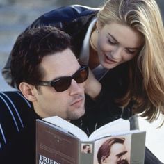 a man reading a book with a woman leaning over him to look at the book