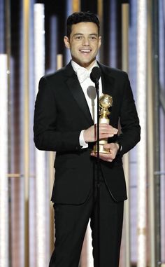 a man in a tuxedo holding an award for best performance by an actor