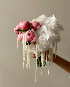 a bouquet of flowers is being held by a person's hand in front of a white wall