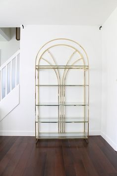 a white room with wood flooring and a gold book shelf on the wall next to an arched doorway