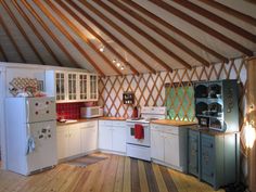 the interior of a yurt kitchen with wood flooring and white cabinets, stove top oven and refrigerator