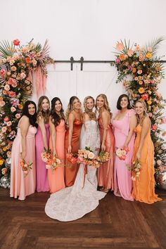 a group of women standing next to each other in front of an arch with flowers