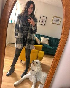 a woman standing in front of a mirror taking a selfie with her white dog